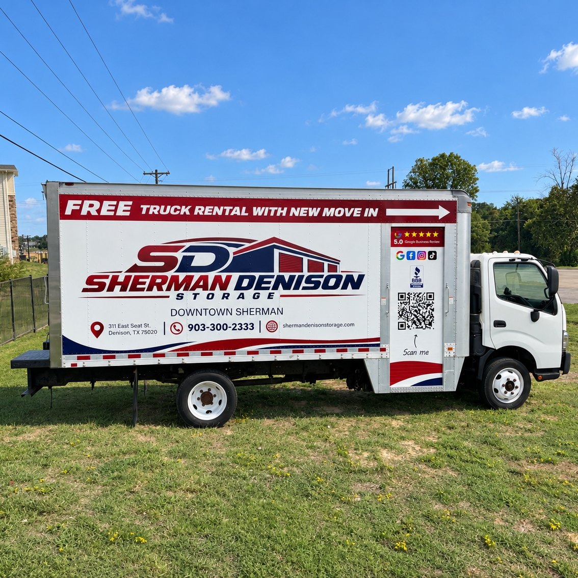 White box truck with a red Free Truck Rental With New Move In banner and the Sherman Denison Storage logo, parked on green grass under a blue sky